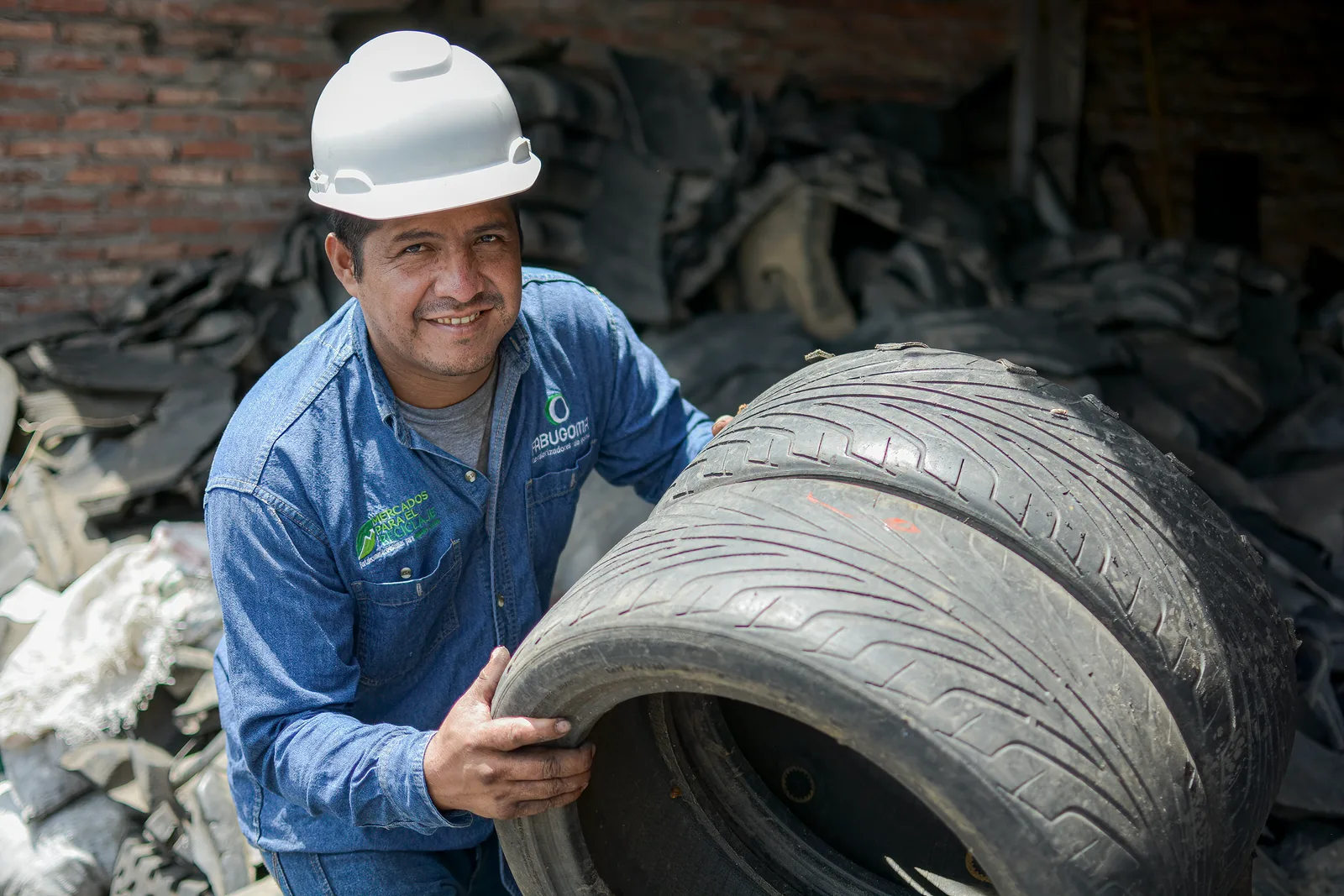 Operario con casco sostiene un neumático en una planta de reciclaje de caucho